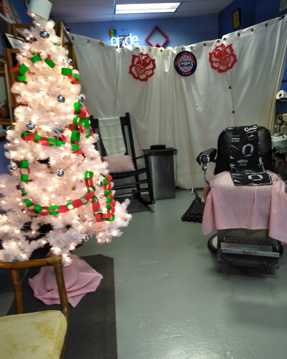A corner of the shop with a white holiday tree, a pride sign and a classic barber chair.